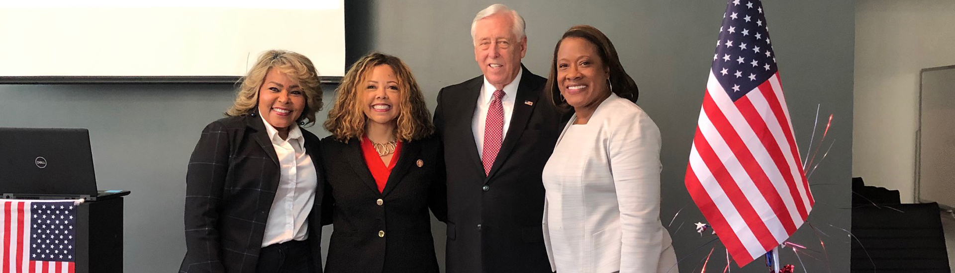 Hoyer standing with other professionally dressed women by an American flag